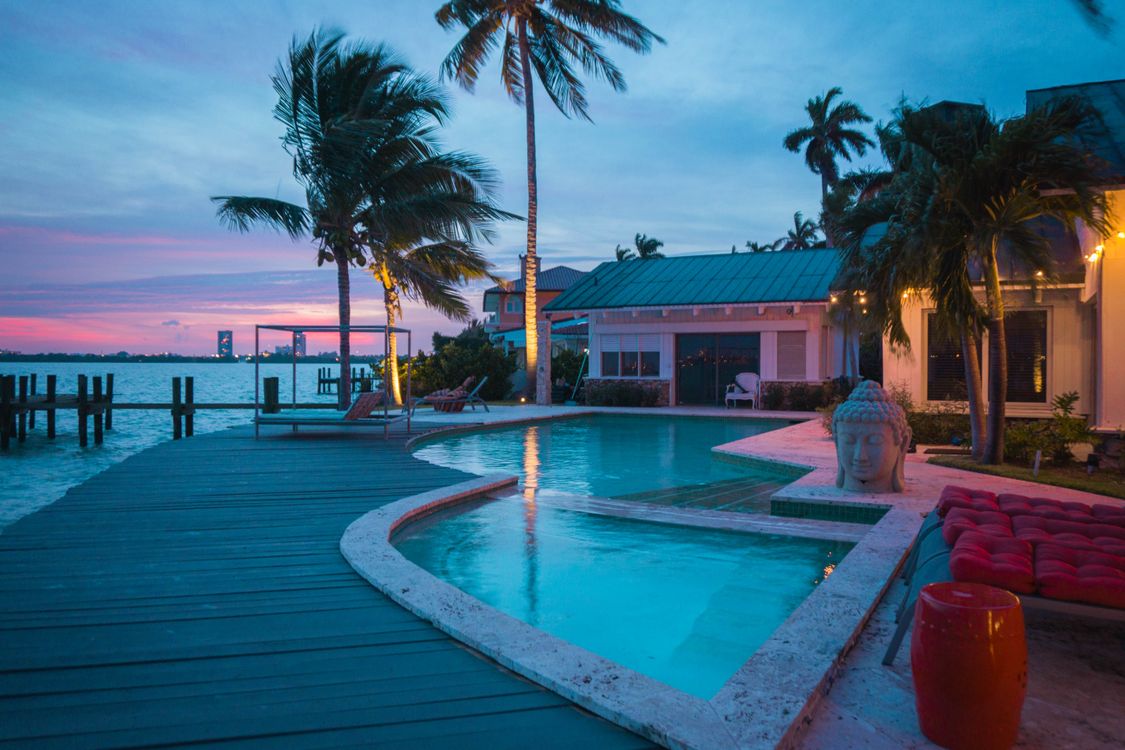 Waterfront single-family home in Miami with a pool, dock, and palm trees at dusk in Florida