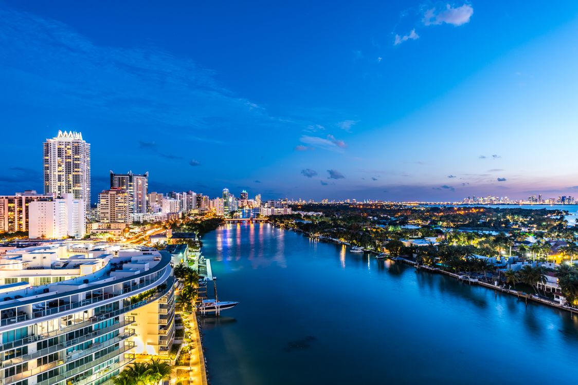 Miami Beach waterfront branded luxury condo towers lit at dusk over the bay in Florida