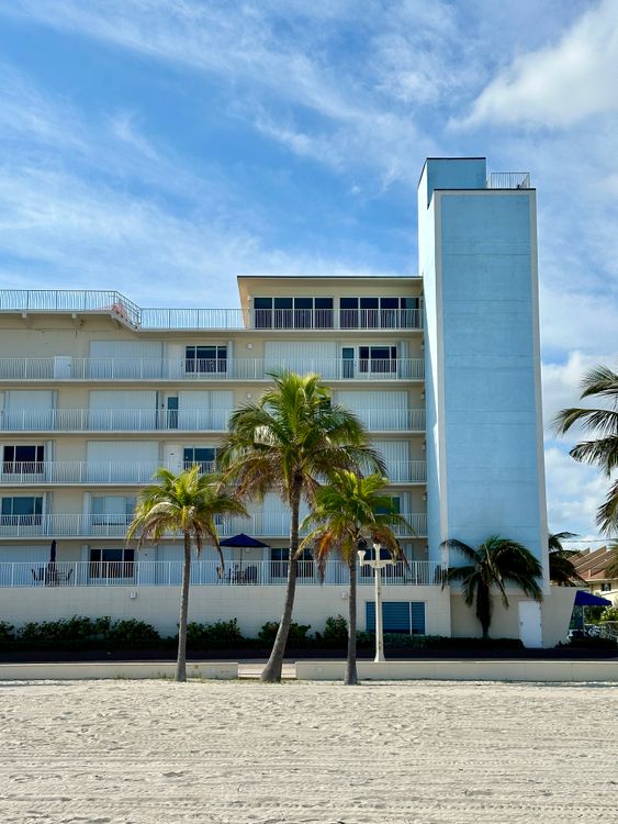 Beachfront branded condo tower in Surfside, Miami, viewed from the sand with palm trees