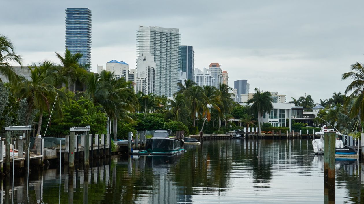 Boats docked along a Miami waterway with condo towers rising behind the palm trees