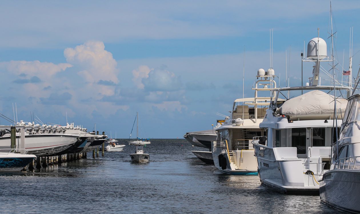 Large luxury yachts berthed at a Miami marina with smaller boats on lifts across the channel