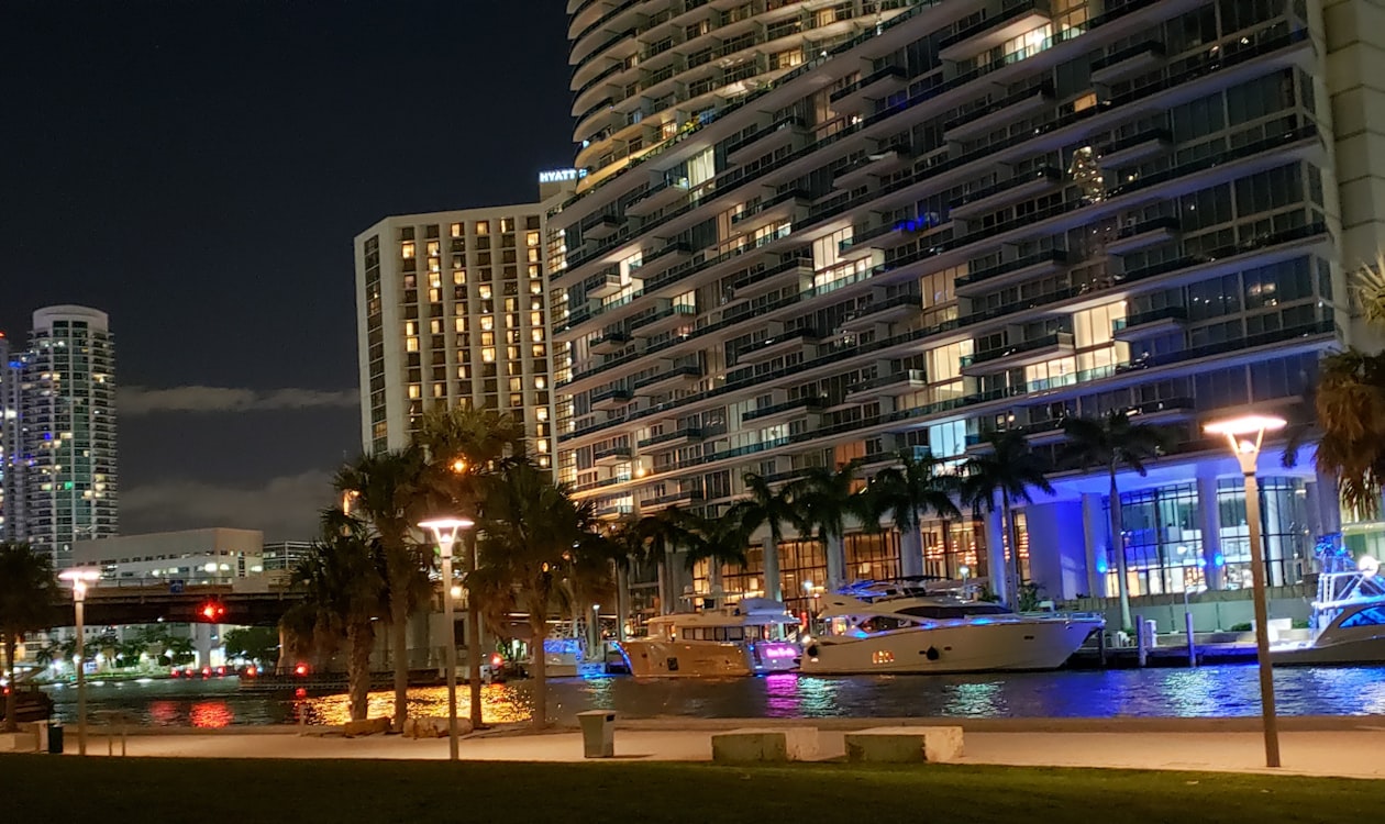 Miami waterfront residential condominium tower lit at night with yachts on the water below