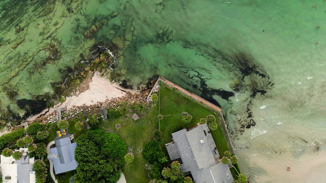 Aerial of a Miami waterfront estate with a private lawn and seawall on turquoise Biscayne Bay