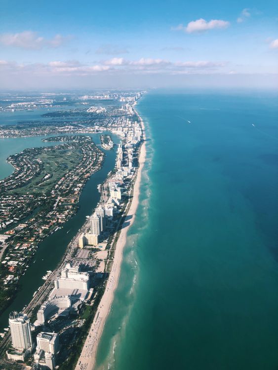 High-altitude aerial of the Miami Beach barrier island with waterfront homes between Biscayne Bay and the Atlantic