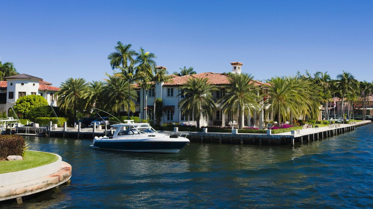 South Florida waterfront mansion with palm trees and a private yacht dock on a calm canal