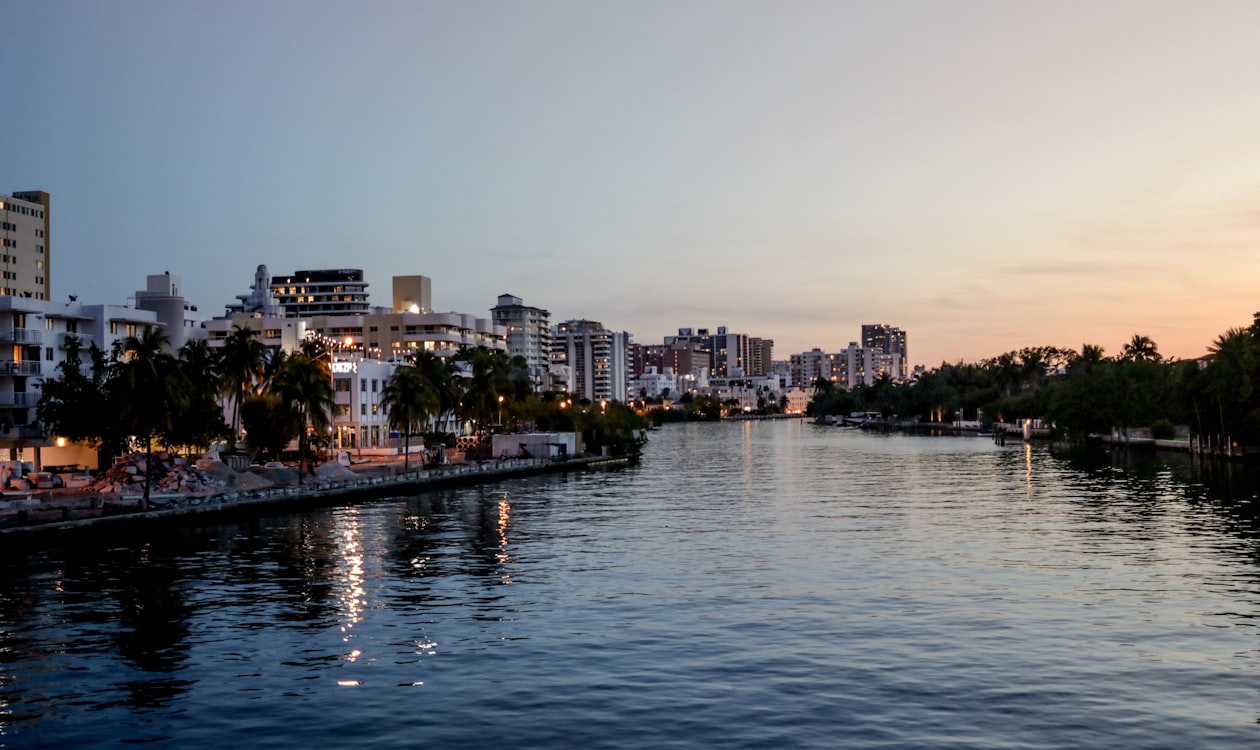 Miami Beach waterfront condos and palm-lined shoreline at dusk along a calm bay channel