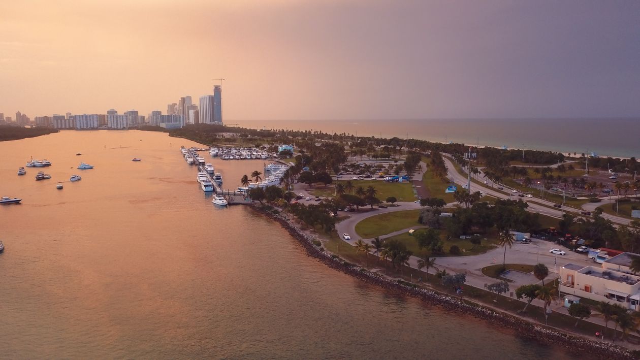 Aerial view at golden hour of a North Miami Beach inlet marina with Sunny Isles towers on the horizon, near Golden Beach