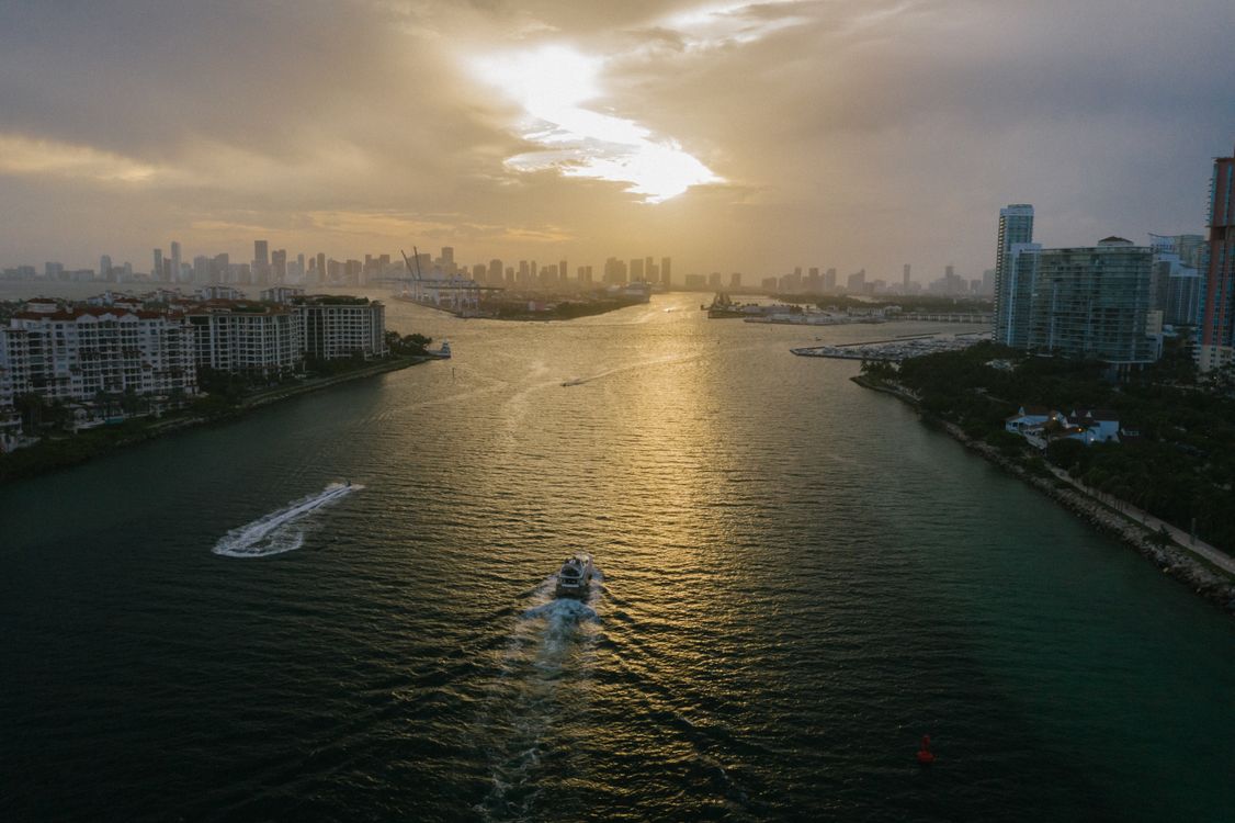 Aerial view of the shipping channel between Miami Beach and the downtown Miami skyline at sunset, with condominium towers along both shores