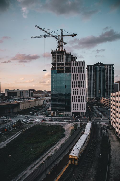 A South Florida condominium tower under construction at dusk with a tower crane above the unfinished top floors