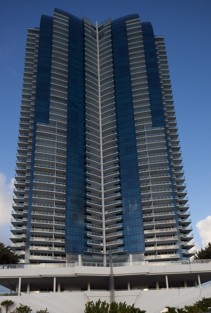 Oceanfront luxury high-rise condominium tower with blue glass and curved balconies in a Sunny Isles Beach style setting on the Atlantic