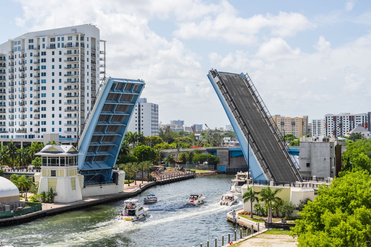 A South Florida drawbridge raised over a river with boats passing between waterfront residential buildings