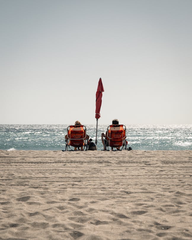 Beachgoers relaxing under an umbrella on the sand at Hollywood Beach, Florida, facing the Atlantic Ocean