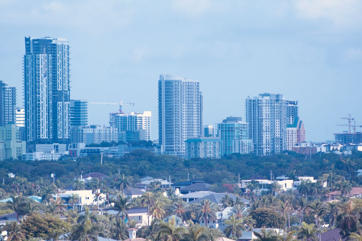South Florida condo towers rising directly behind a low-rise palm neighborhood, the two markets that price per square foot measures differently