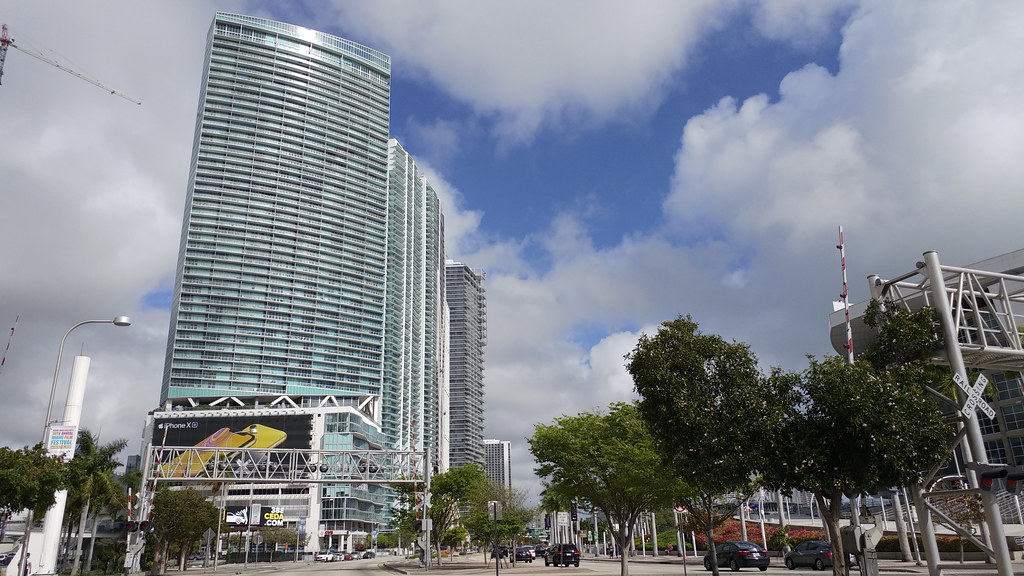Miami residential condo towers under a partly cloudy sky with a construction crane rising behind them