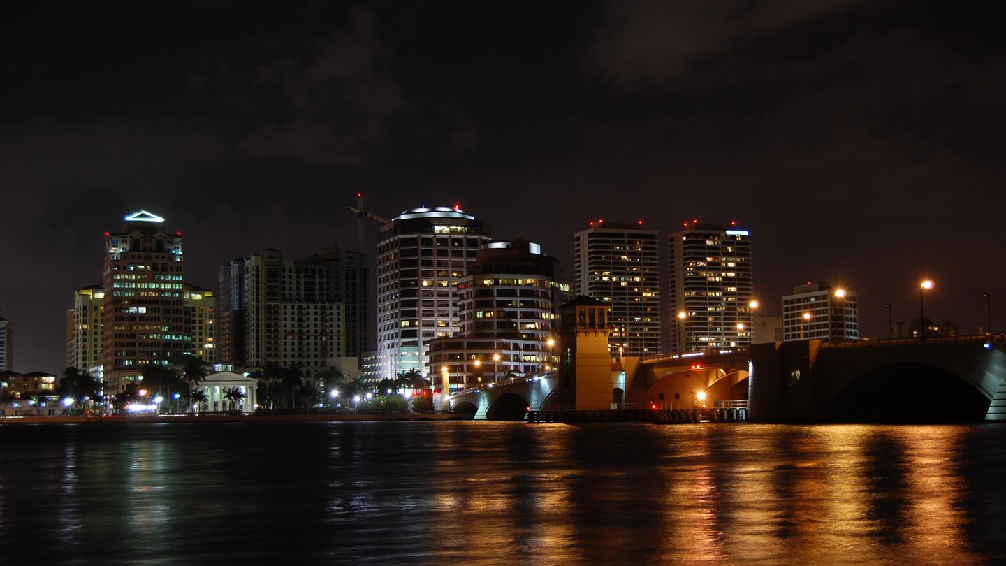 The West Palm Beach skyline lit at night across the Intracoastal Waterway with the Royal Park Bridge in the foreground