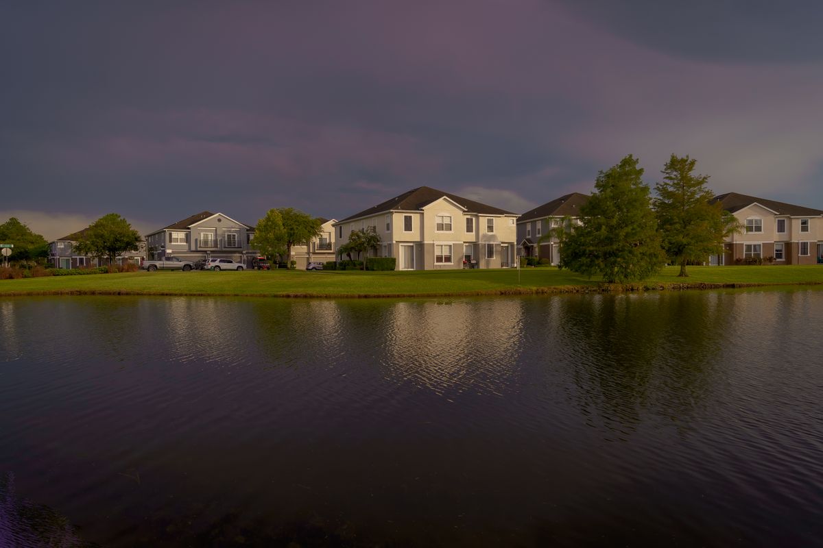 Lakefront Florida homes reflected in still water under a dramatic sky, representative of the lake-lined western Broward setting around Weston